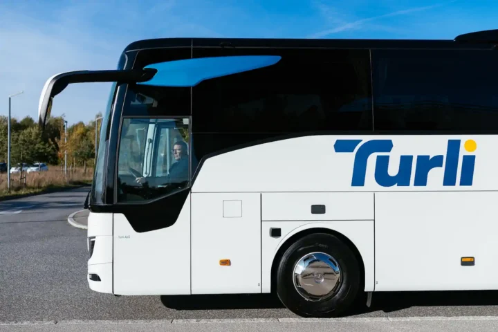Hvid Turli turistbus set fra siden med turkis logo på.